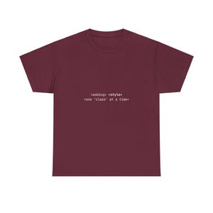 May include: A maroon t-shirt with the text "<adding> <style> <one 'class' at a time>" printed in white. The shirt is a crew neck style and appears to be made of a soft material.