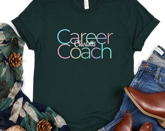 May include: A dark green t-shirt with the text "Career Coach" in rainbow colours. The name "Charlotte" is written in a smaller font below the text.