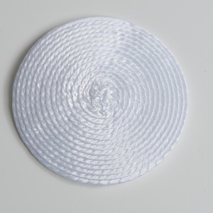 May include: A circular white coaster or mat constructed from a continuous, tightly coiled synthetic rope. The material features a smooth, glossy finish with a distinct braided texture that spirals outward from the center to the edge.