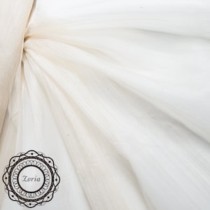 May include: White sheer fabric with a subtle shimmer. The fabric is draped and folded, creating soft folds and wrinkles. The fabric is lightweight and translucent.