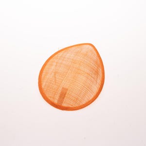 May include: A teardrop-shaped fascinator base crafted from a vibrant orange woven sinamay material. The accessory features a fine, grid-like texture throughout its surface and a reinforced, matching orange fabric trim along the entire outer edge.