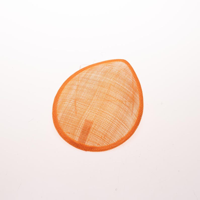 May include: A teardrop-shaped fascinator base crafted from a vibrant orange woven sinamay material. The accessory features a fine, grid-like texture throughout its surface and a reinforced, matching orange fabric trim along the entire outer edge.