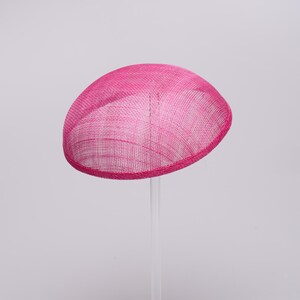 May include: A bright hot pink fascinator hat with a smooth, rounded dome shape. The hat is constructed from a fine, woven mesh material that features a visible cross-hatched texture throughout the surface, finished with a clean, bound edge.