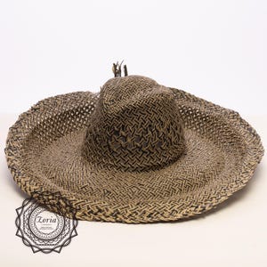 May include: A wide-brimmed sun hat with a woven design in shades of brown and black. The hat features a structured crown and a wide, floppy brim. The hat is made of a natural fiber material, perfect for sun protection.