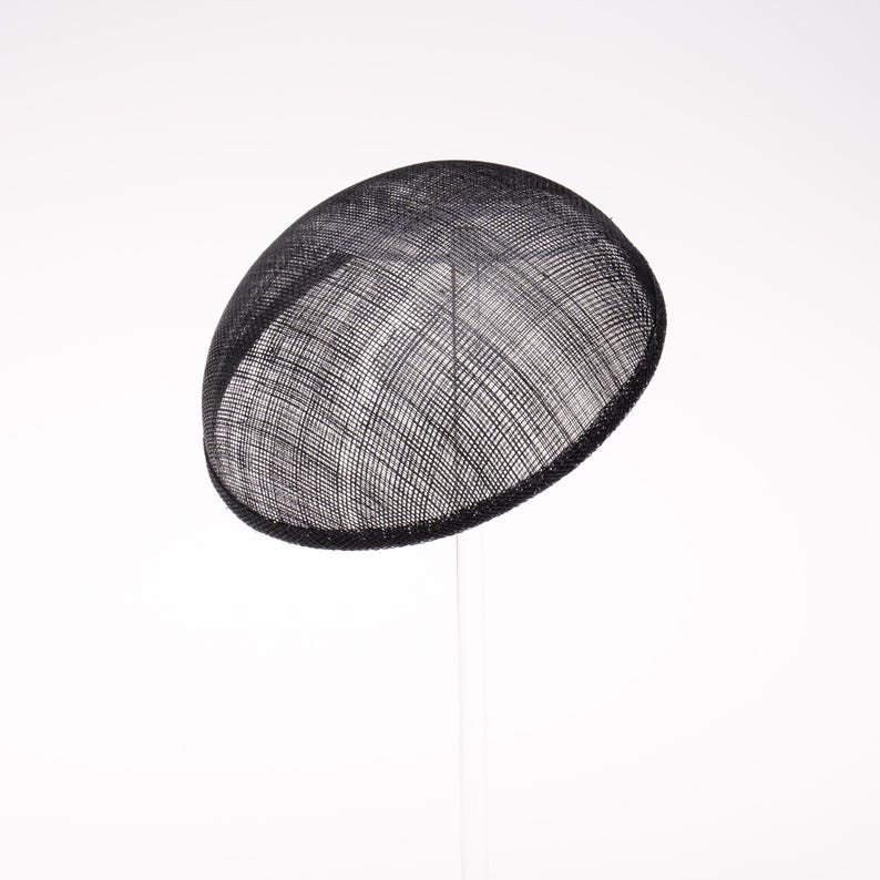 May include: A black fascinator hat with a rounded, dome-shaped silhouette. The headpiece is crafted from a fine, woven mesh material that features a visible grid-like texture throughout the surface, creating a semi-sheer appearance.