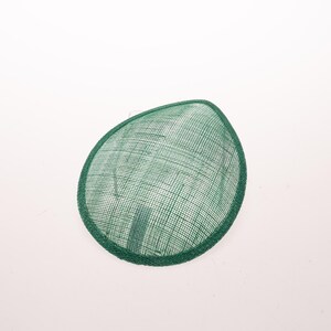 May include: A teardrop-shaped fascinator hat in a vibrant emerald green color. The headpiece features a fine, woven mesh texture throughout its surface, finished with a matching green fabric trim along the entire outer edge of the curved frame.