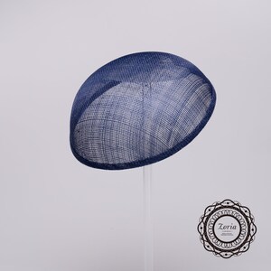 May include: A deep navy blue dome-shaped fascinator hat crafted from a stiffened, woven mesh material. The hat features a smooth, rounded silhouette and a clean, finished edge. In the bottom right corner, a circular logo reads Zoria.