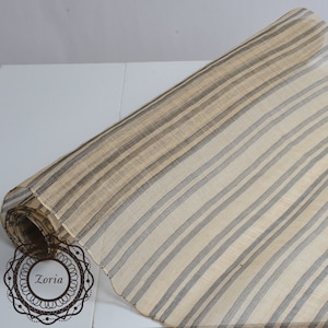 May include: A roll of beige and gray striped fabric. The fabric has a woven texture and is rolled up on a white surface.