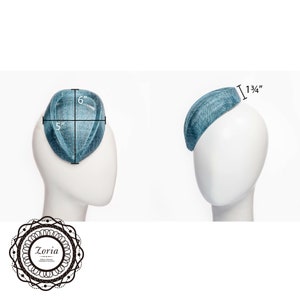 Op de afbeelding: Een blauwgroene, druppelvormige fascinatorhoed met een geweven textuur. De hoed is 6 inch lang, 5 inch breed en 1,75 inch hoog. Het Zoria-logo wordt weergegeven in een cirkelvormig decoratief kader in de linkerbenedenhoek.