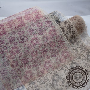 May include: Three rolls of sheer fabric with a floral pattern. The fabric is beige with a pink and gray floral design. The fabric is sheer and has a delicate texture.