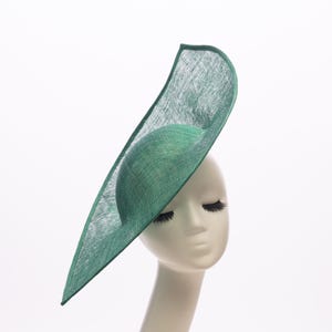 May include: A green hat with a dramatic, asymmetrical design. The hat features a rounded crown and a wide, elongated brim that extends upwards. The hat is displayed on a mannequin head against a white background.