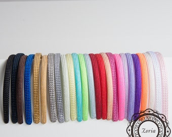 May include: A collection of twenty-four fabric-covered headbands arranged in a row, featuring a spectrum of colors including black, brown, blue, gold, silver, yellow, green, red, pink, purple, orange, and white. A logo with the text Zoria is visible.