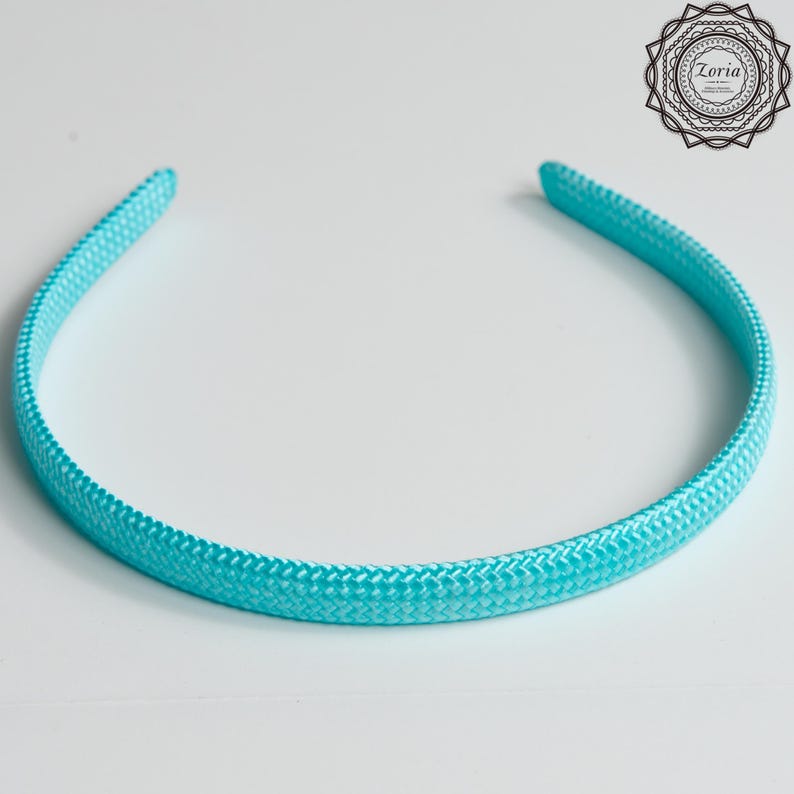 Pu&ograve; includere: Una fascia per capelli turchese con una trama intrecciata. L'accessorio per capelli &egrave; una semplice fascia curva, progettata per essere indossata sulla fronte. La fascia &egrave; di un colore pieno e brillante ed &egrave; probabilmente realizzata in tessuto o materiale simile.