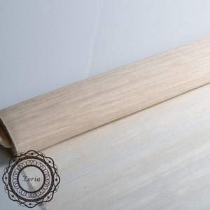 May include: A rolled-up, light-colored wood-grain patterned material. The material is a light beige color with darker wood grain lines. The material is on a light-colored surface. The image includes the text "Zoria" in a decorative circular frame.