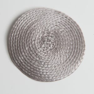 May include: A circular coaster featuring a light gray, metallic-toned rope coiled in a continuous spiral pattern. The rope is tightly wound from the center outward, creating a textured, concentric design with a subtle sheen throughout.
