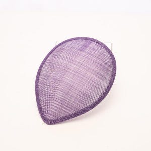 May include: A teardrop-shaped fascinator base in a vibrant purple hue, featuring a fine, woven mesh texture throughout. The piece is finished with a matching purple bound edge that defines its distinct, curved silhouette and structured form.