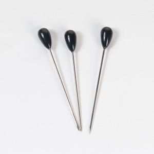 May include: Three black-headed pins with silver metal shafts.