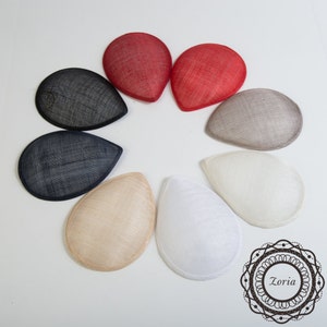 May include: Eight teardrop-shaped hat bases in various colors, including black, white, beige, and red. The bases are made of a woven material and are arranged in a circle on a white background.