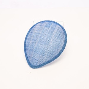 May include: A teardrop-shaped fascinator hat in a vibrant blue color. The headpiece features a fine, woven mesh texture throughout its surface, with a solid blue bound edge that defines its distinct, asymmetrical, and curved silhouette.