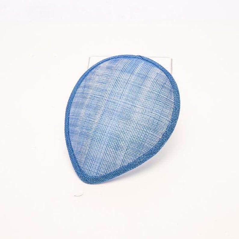May include: A teardrop-shaped fascinator hat in a vibrant blue color. The headpiece features a fine, woven mesh texture throughout its surface, with a solid blue bound edge that defines its distinct, asymmetrical, and curved silhouette.