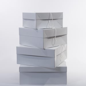 May include: A stack of five white, rectangular boxes. Each box has a lid and is tied with a white string. The boxes are arranged in a vertical stack, with the largest box at the bottom and the smallest at the top. The boxes are plain and unadorned.
