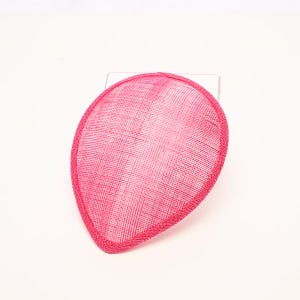 May include: A teardrop-shaped fascinator base in a vibrant hot pink color. The accessory features a woven, textured fabric construction with a distinct cross-hatch pattern throughout the surface and a reinforced, matching pink piped edge border.