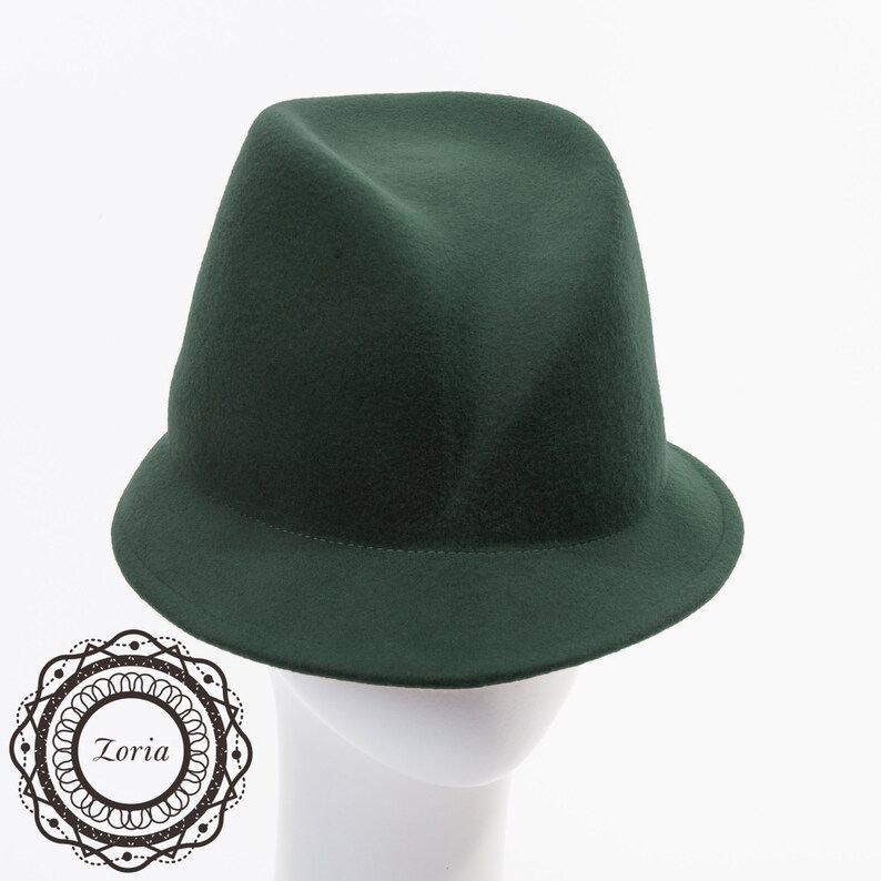 May include: A dark green felt fedora hat with a wide brim. The hat is sitting on a white mannequin head.