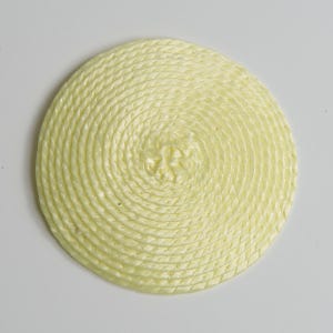 May include: A circular coaster made of pale yellow rope coiled in a tight spiral pattern. The rope has a twisted texture and is arranged to form a flat, round shape with a consistent thickness throughout the entire surface of the object.