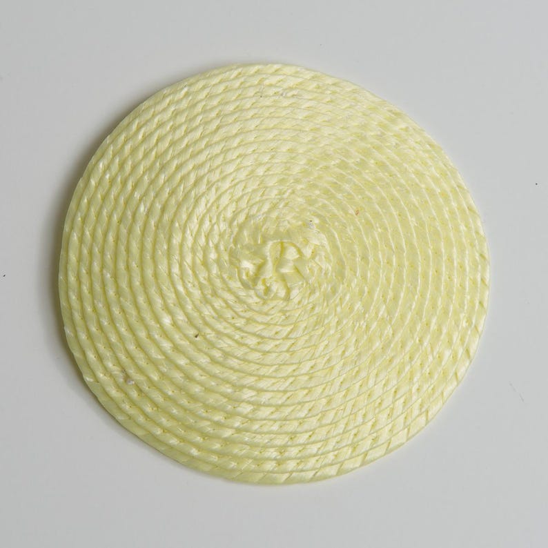 May include: A circular coaster made of pale yellow rope coiled in a tight spiral pattern. The rope has a twisted texture and is arranged to form a flat, round shape with a consistent thickness throughout the entire surface of the object.