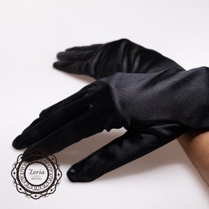 May include: A pair of elegant black gloves made of a smooth, shiny fabric. The gloves are long, covering the wrist and extending up the arm. The gloves are displayed on a white background.