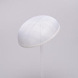 May include: A solid white, dome-shaped hat with a woven, textured surface. The hat features a clean, rounded silhouette and a finished edge, presented on a clear, vertical stand against a plain, light-colored background.