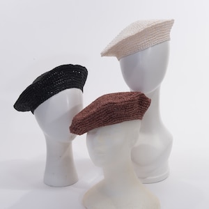 May include: Three straw berets in different colors: black, brown, and white. The berets are displayed on mannequin heads.