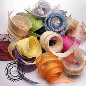 May include: A collection of multi-colored mesh ribbons in shades of yellow, orange, purple, red, blue, green, pink, and beige. The ribbons feature a loose, open-weave texture and are coiled into spirals. A black circular logo with the text Zoria is visible.