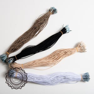 May include: Bundles of elastic cords in various colors: brown, black, beige, and white. Each bundle is secured with a rubber band and has metal tips. The cords are arranged on a white surface.