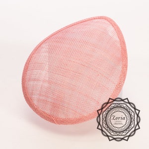 May include: A teardrop-shaped fascinator base in a soft peach-pink hue, crafted from a fine, woven mesh material with a structured, reinforced edge. A black circular logo featuring the text Zoria Millinery Materials, Trimmings & Accessories.