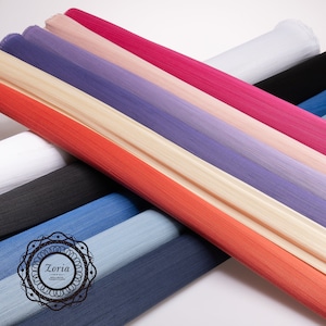 May include: Multiple rolls of sheer tulle fabric in various colors including red, orange, beige, purple, pink, white, black, and shades of blue. A circular black logo with the text Zoria is printed on the lower left side of the fabric rolls.