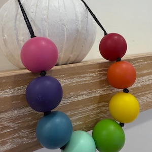 May include: A rainbow coloured beaded necklace with large, round beads. The beads are strung on a black cord.