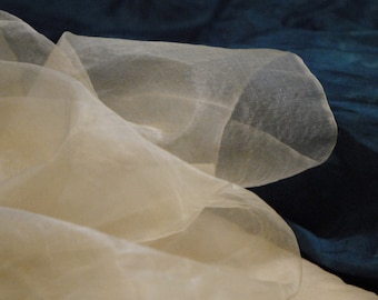 May include: A sheer, white fabric with a delicate, flowing texture. The fabric is draped over a dark blue surface.