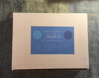 May include: A white box with a blue label that says "Aurora Silk presents Natural Dye Kit INDIGO all-natural fermentation vat". The label also includes a list of what is included in the kit: "Your kit includes: a source of powdered indigo, 4 turns in a stirring stick, a mortar and pestle, a small amount of ground madder root, 1 ounce of wheat bran, 1 ounce "Tonic Mix", five 4" x 5" squares of silk, wool, silk cotton, wool, and wood."