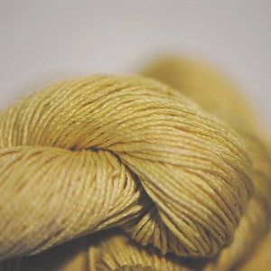 May include: Close-up of a knot of pale yellow yarn. The yarn is soft and textured, with a subtle sheen.
