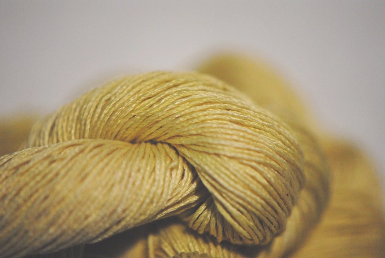 May include: Close-up of a knot of pale yellow yarn. The yarn is soft and textured, with a subtle sheen.