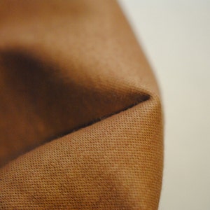 May include: Close-up of a brown fabric with a textured surface. The fabric is folded over, creating a crease.