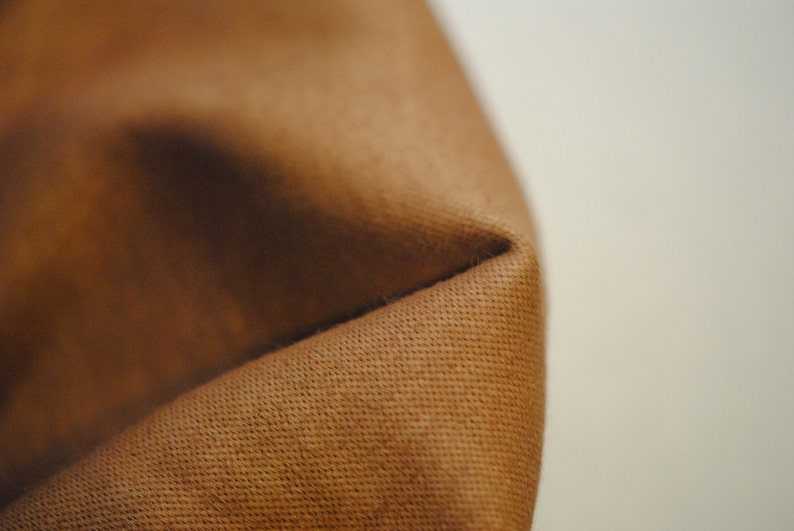 May include: Close-up of a brown fabric with a textured surface. The fabric is folded over, creating a crease.