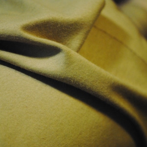 May include: Close-up of a soft, beige fabric with a textured surface. The fabric is folded and draped, creating a smooth, flowing look.