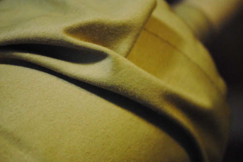 May include: Close-up of a soft, beige fabric with a textured surface. The fabric is folded and draped, creating a smooth, flowing look.