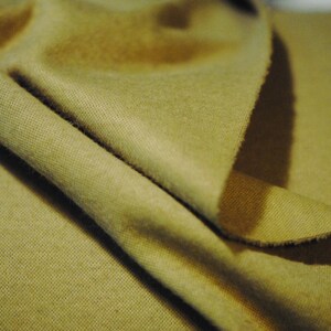 May include: A close-up of a folded piece of fabric in a muted olive green color. The fabric has a soft, textured surface.