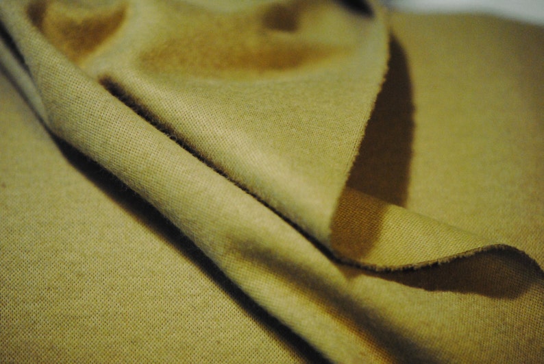 May include: A close-up of a folded piece of fabric in a muted olive green color. The fabric has a soft, textured surface.