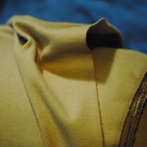 May include: A close-up of a folded piece of fabric. The fabric is a light beige color and has a soft, fuzzy texture. The fabric is folded in a way that creates a series of overlapping layers.