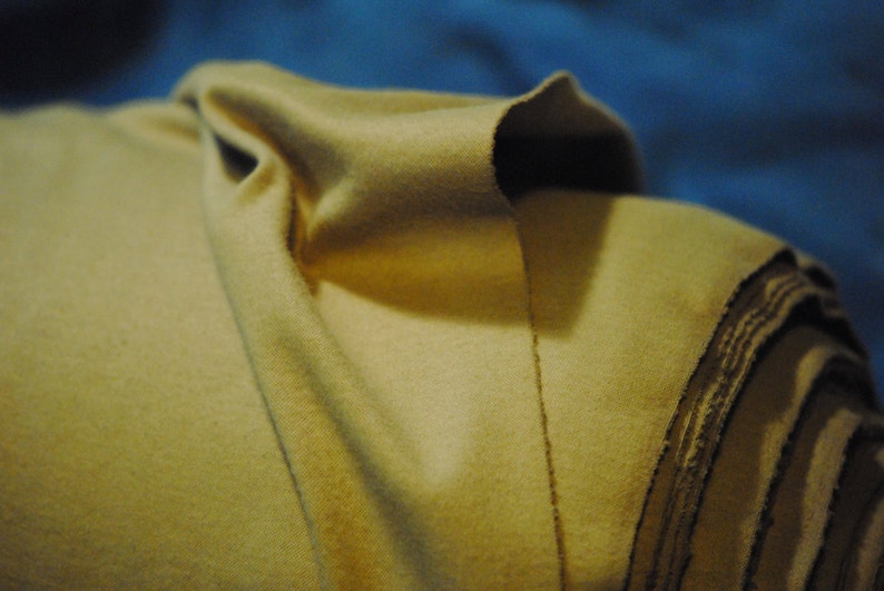 May include: A close-up of a folded piece of fabric. The fabric is a light beige color and has a soft, fuzzy texture. The fabric is folded in a way that creates a series of overlapping layers.