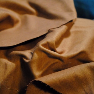 May include: A close-up of a brown fabric with a soft, textured surface. The fabric is folded and draped, creating a sense of depth and dimension.